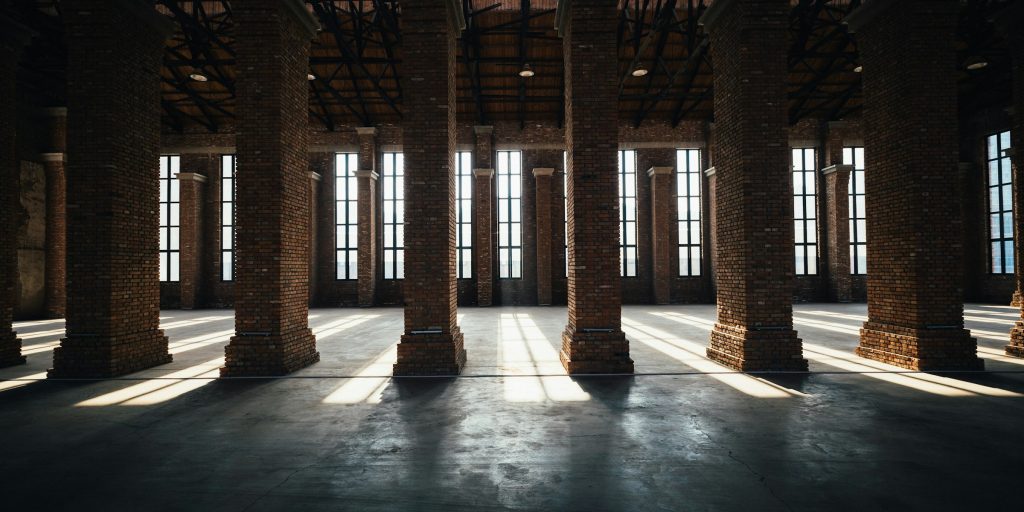 Sunlight streaming through tall warehouse windows onto brick columns